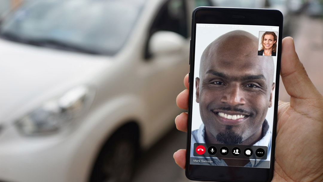 auto-dealership man holding a phone doing video conferencing with a car background