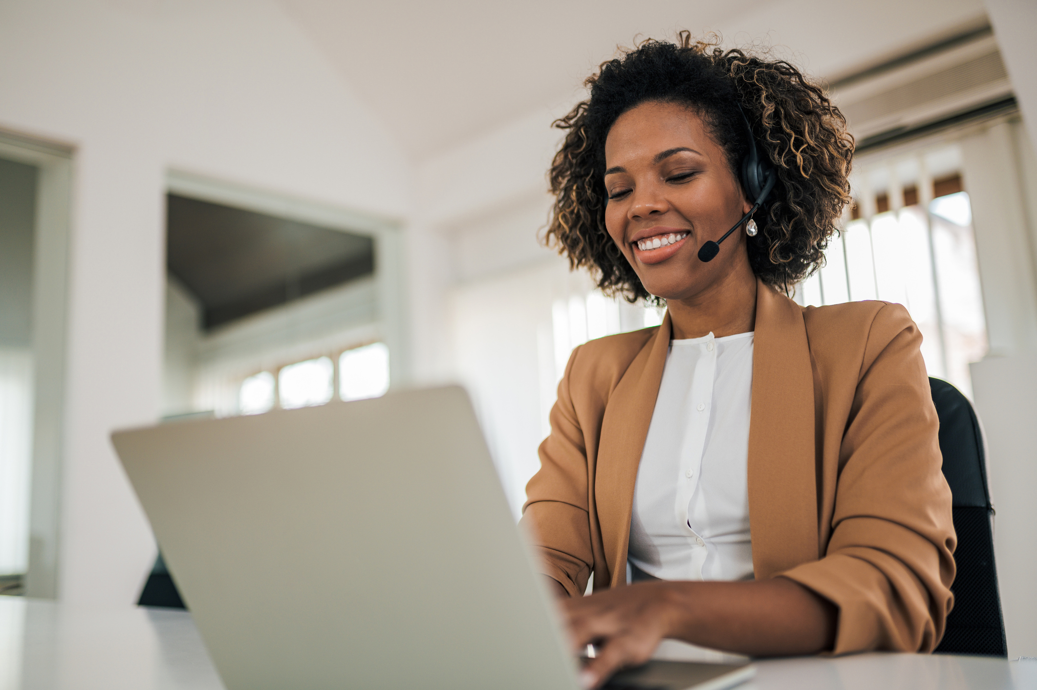 Low angle portrait of a happy woman wearing headset using laptop.