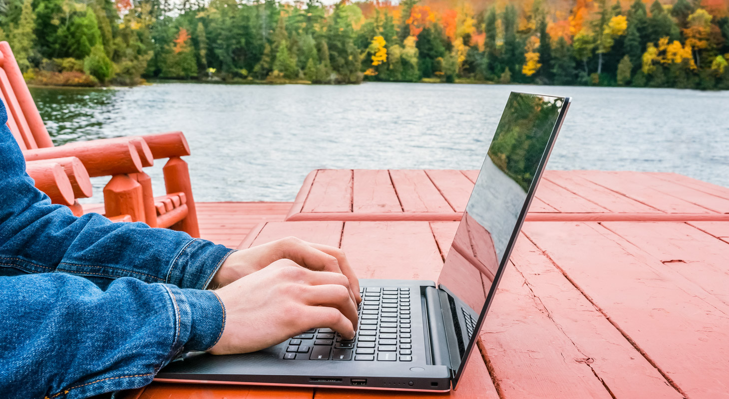 Adult male hands - digital nomad taking advantage of outdoors in autumn - working on laptop by the edge of a lake. Blurred background - autumn colors People Using Mobile Devices
